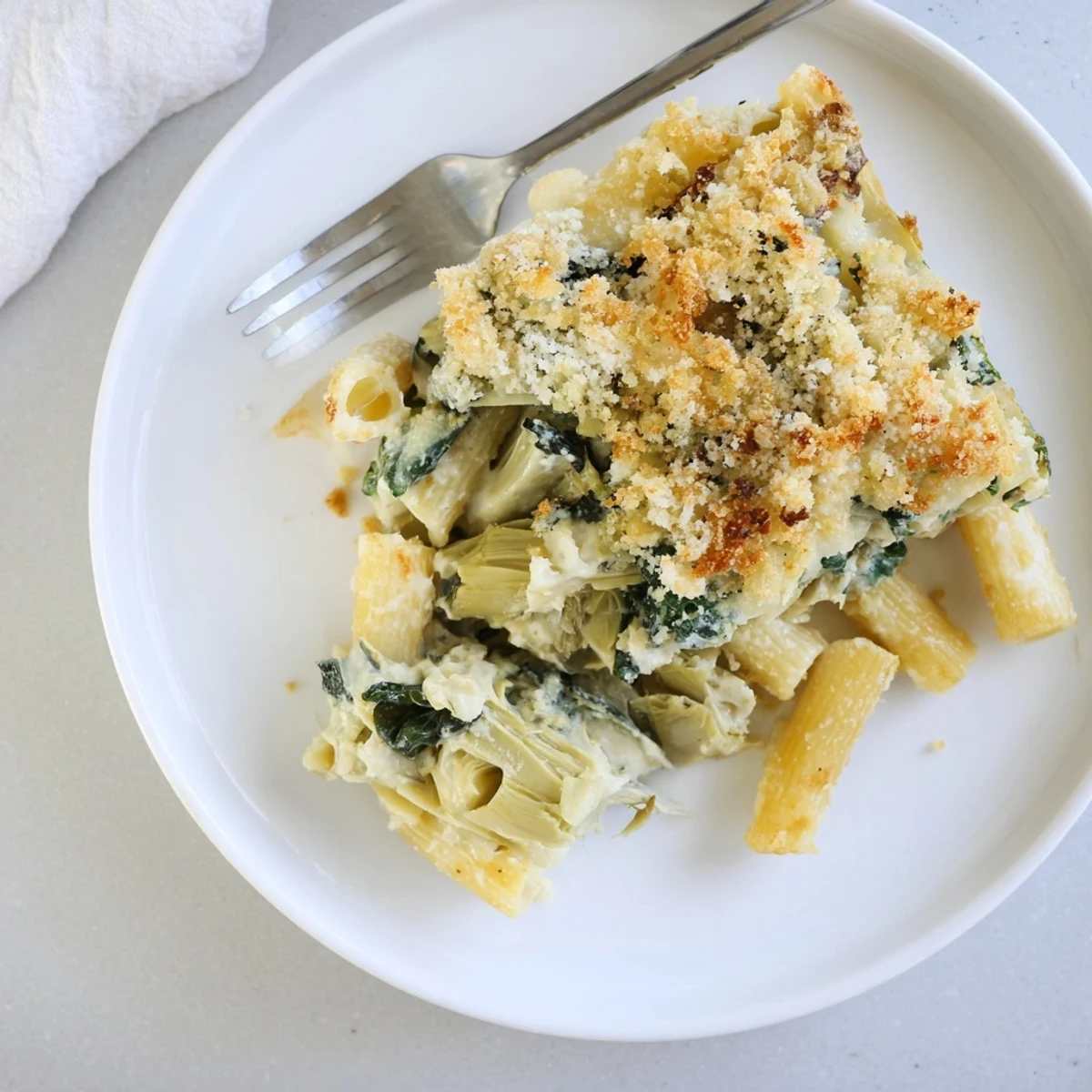 A serving of Artichoke Pasta Bake on a plate, ready to eat, with steam rising from the rich, cheesy cream sauce.