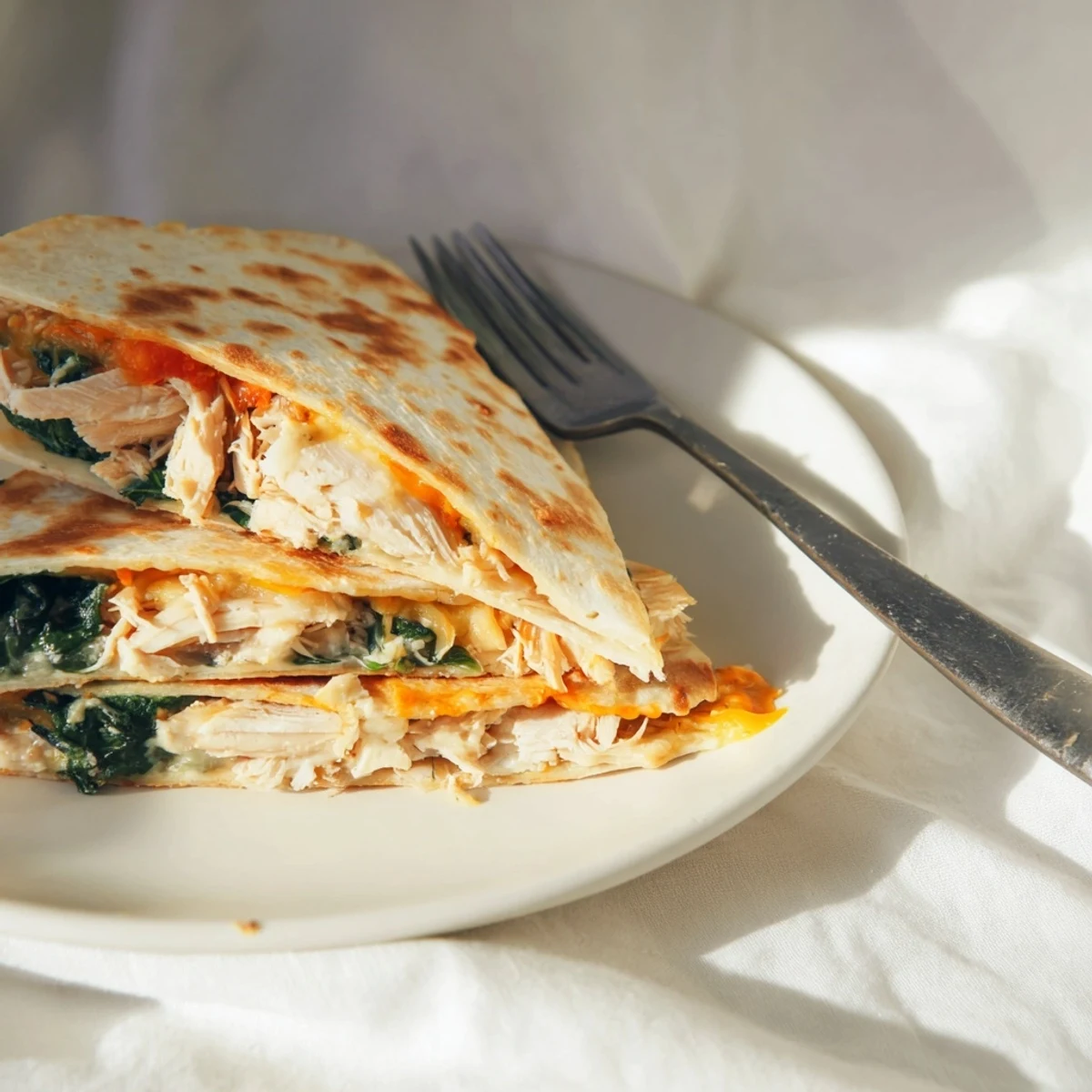 A golden-brown Chicken and Spinach Quesadilla wedges on a white plate, melted mozzarella stretching between layers of savory chicken and tender spinach.