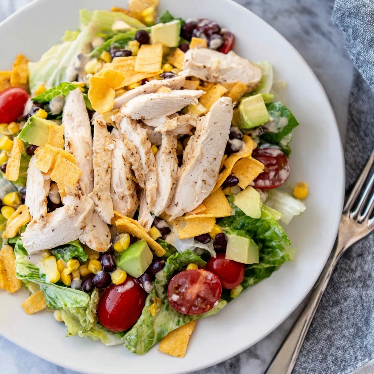 A close-up of Crunchy Taco Chicken Salad shows seasoned chicken, fresh veggies, and crushed shells on a bed of crisp romaine.  