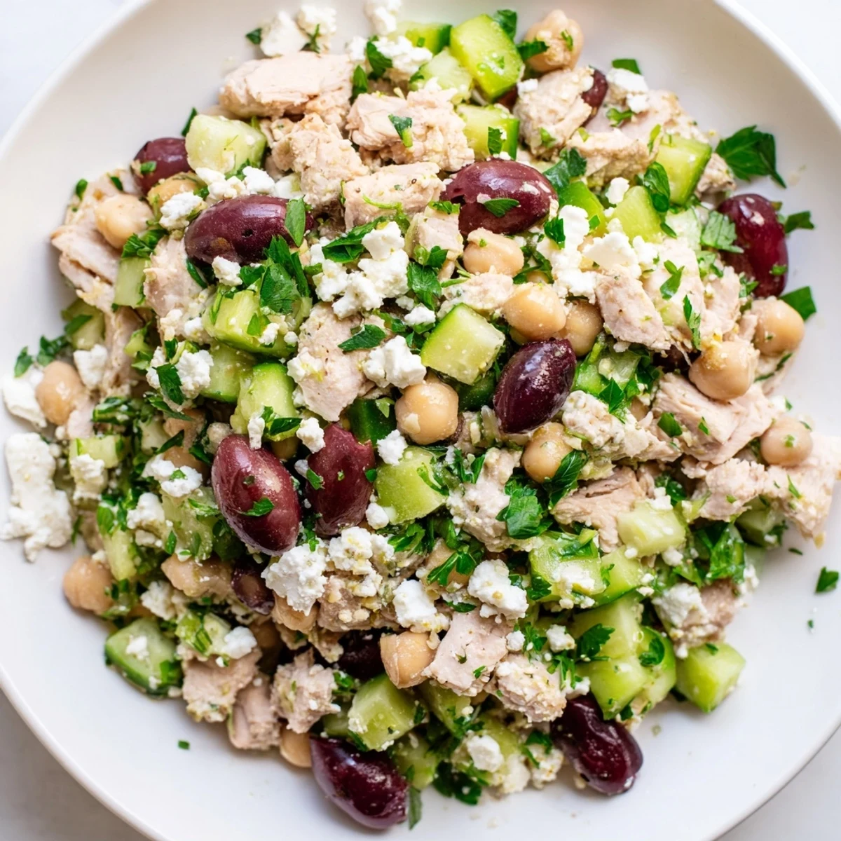 A close-up of Mediterranean Chickpea Chicken Salad shows juicy chicken, creamy feta, and crisp veggies drizzled with zesty dressing.