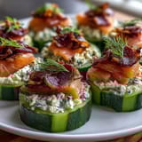 Cucumber bites with cream cheese and smoked salmon, arranged on a white platter with dill and capers for a fresh appetizer.