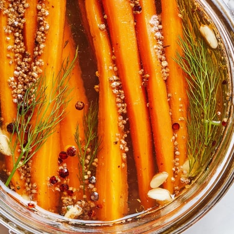 Quick pickled carrot spears, vibrantly orange, swimming in a clear, tangy brine in a jar.