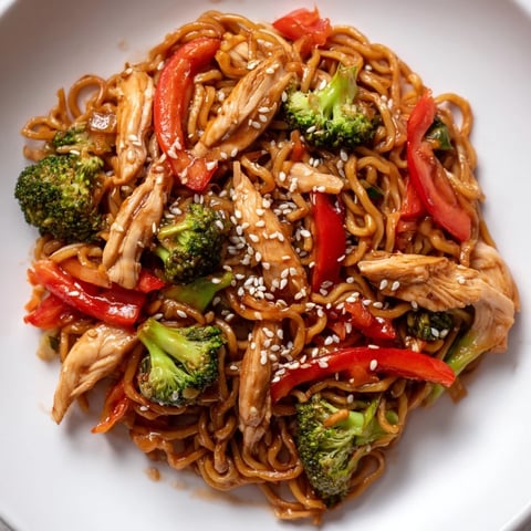 Steaming bowls of Spicy Ramen Stir-Fry feature tender chicken strips, crisp bell peppers, and broccoli tossed in a glossy, fiery red sauce.  