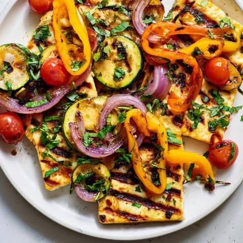 Thick, perfectly grilled halloumi cheese steaks arranged beside vibrant roasted vegetables and halved cherry tomatoes, ready to serve with a drizzle of olive oil.  