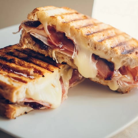 The pressed Crispy Prosciutto & Fig Panini sits on a rustic wooden board, ready to be enjoyed warm with its crisp crust.