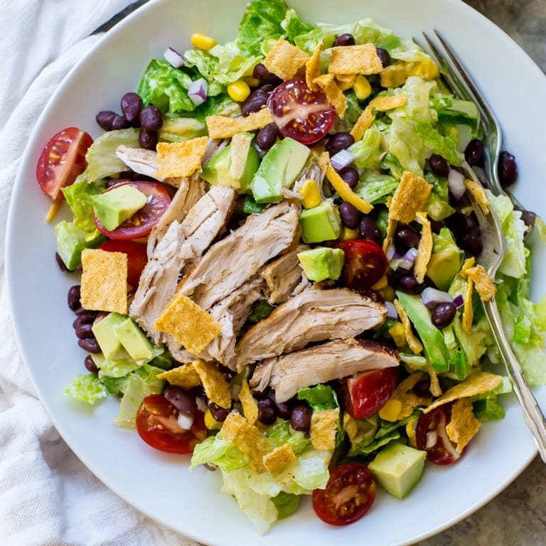 Ready-to-eat Crunchy Taco Chicken Salad in a white bowl, topped with cheddar, avocado, and a drizzle of creamy lime dressing.  