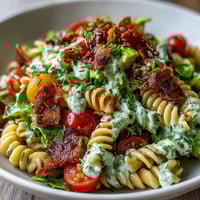 Vibrant BLT pasta salad with crispy bacon, juicy tomatoes, and creamy avocado ranch dressing, served in a white bowl.  